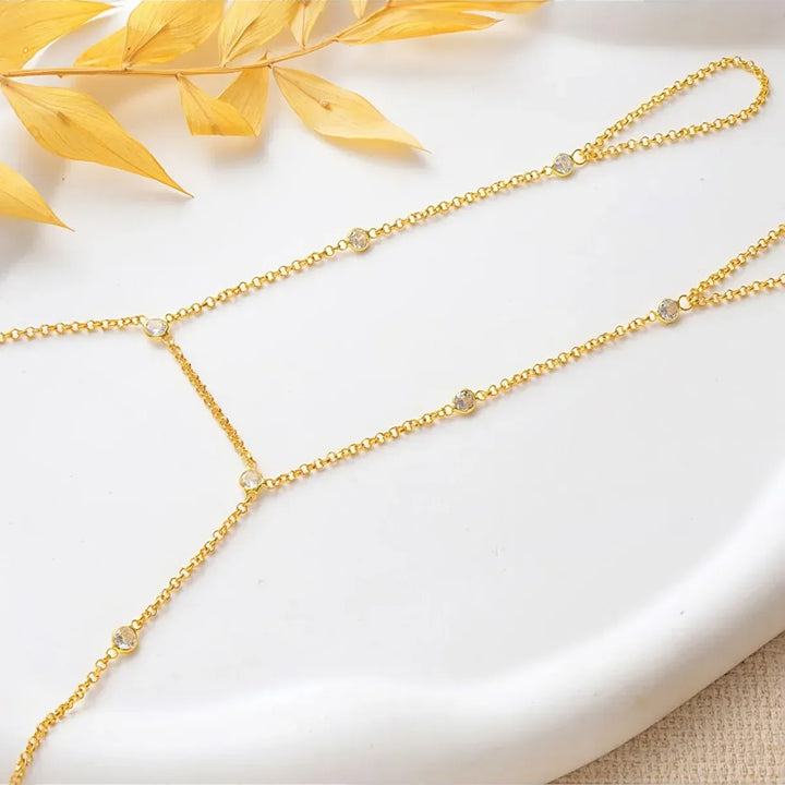 Gold-plated hand chain on a white surface with yellow leaves