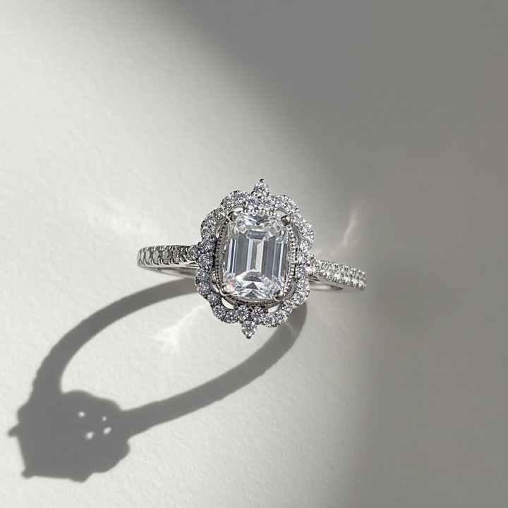 Diamond ring with a central gemstone and halo on a reflective surface