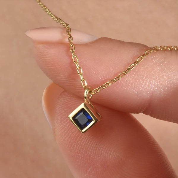 Gold necklace with a blue gemstone pendant held by a hand against a beige background
