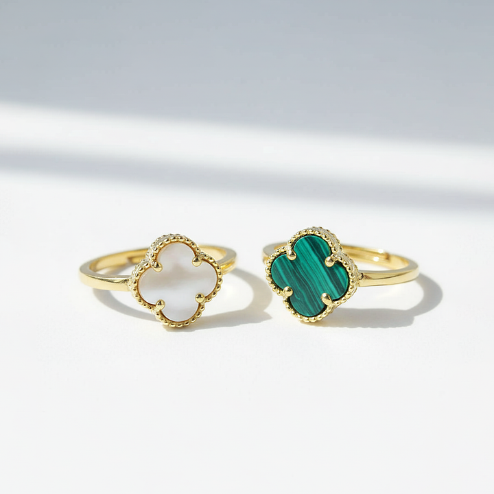 Two gold rings with clover-shaped gemstones on a light gray background