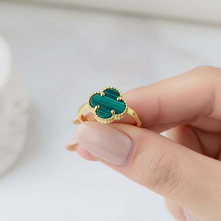 Gold ring with green malachite stone held by a hand on a light background