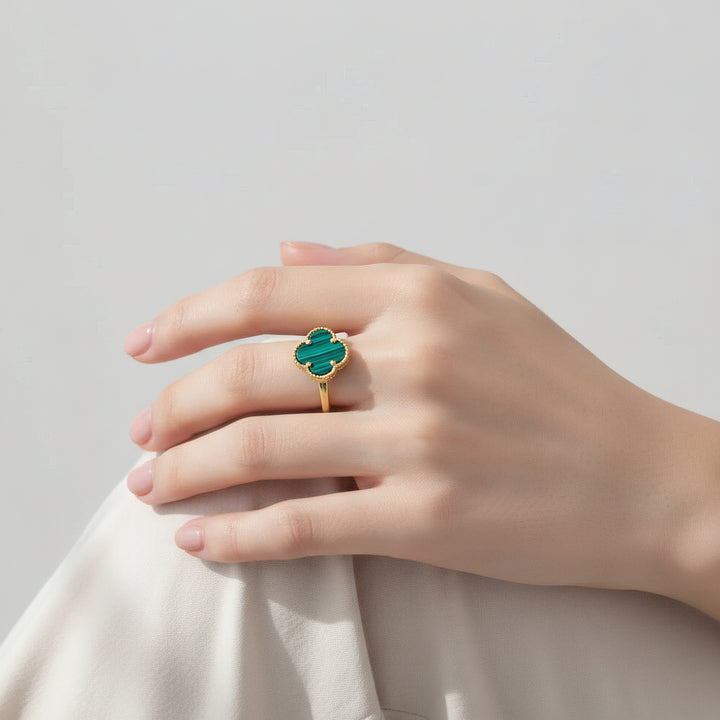 Hand wearing a gold ring with a green gemstone on a light gray background