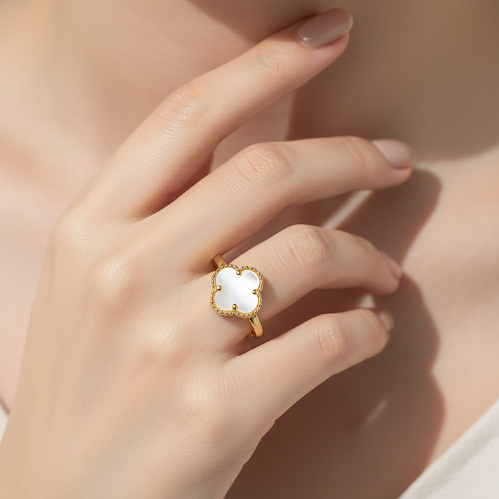 Gold ring with a white mother of pearl stone on a hand against a neutral background