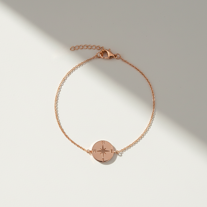 Rose gold bracelet with a compass charm on a light background