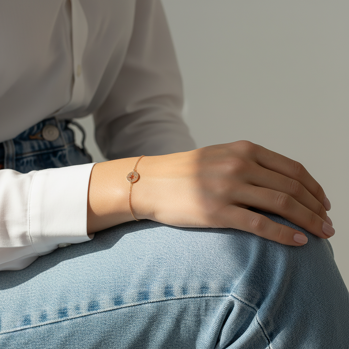 Person wearing a rose gold compass charm bracelet on a light gray background