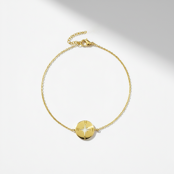 Gold bracelet with a compass-shaped charm on a light gray background
