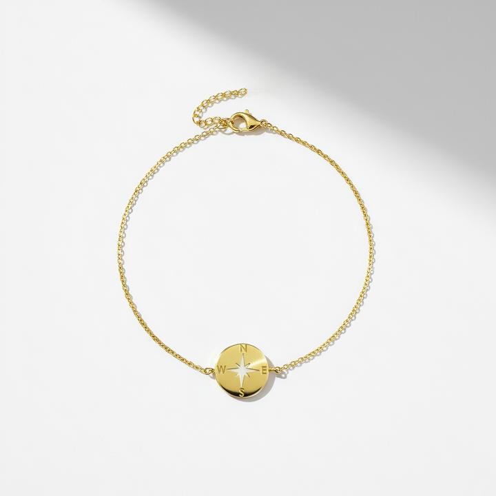 Gold bracelet with a compass-shaped charm on a light gray background