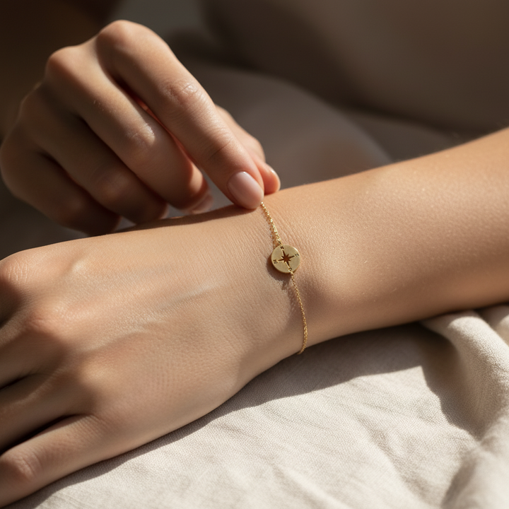 Gold compass bracelet on a wrist with a neutral background