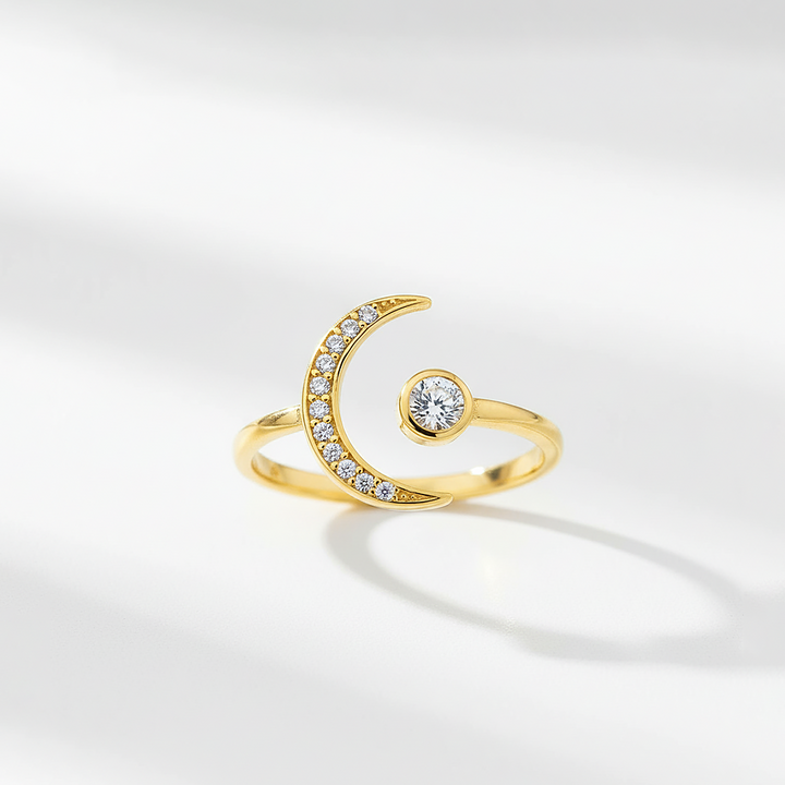 Gold ring with a crescent moon design and small gemstone on a light gray background