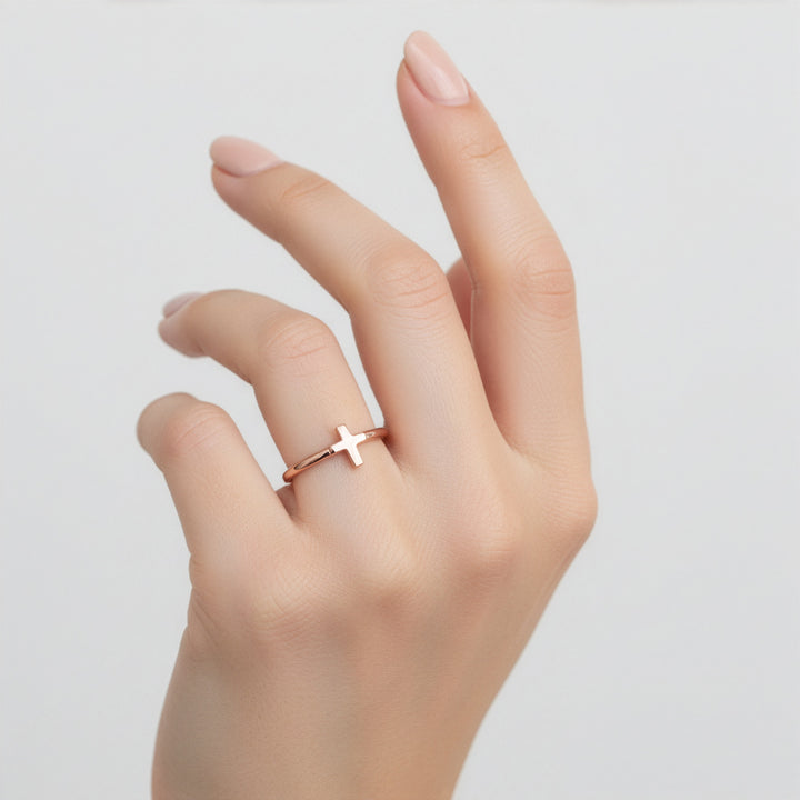 Hand wearing a rose gold cross ring on a light gray background
