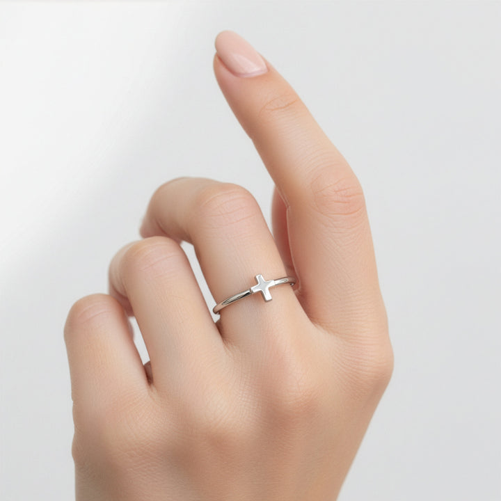 Silver cross ring on a finger against a light gray background