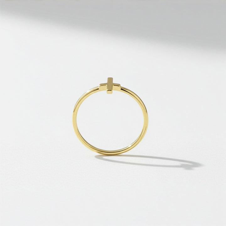 Dainty gold cross ring on a light gray background
