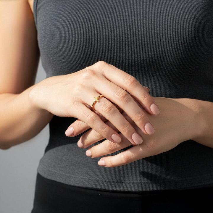 Close-up of a person wearing dainty gold-plated ring on a plain background