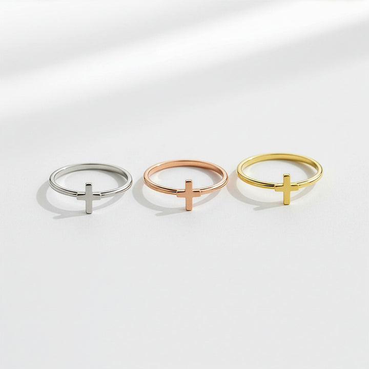 Three rings with cross designs in silver, rose gold, and yellow gold on a light gray background.