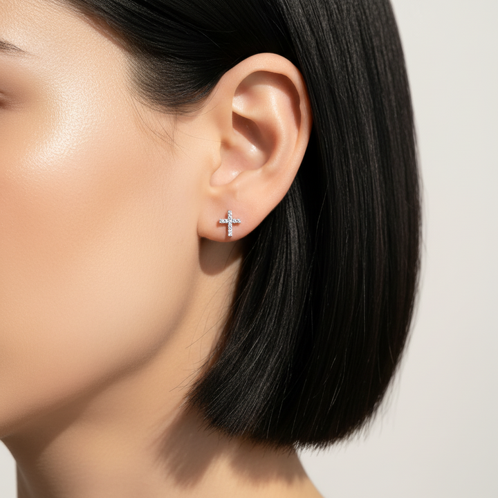 Close-up of an ear wearing a small cross earring with a plain background