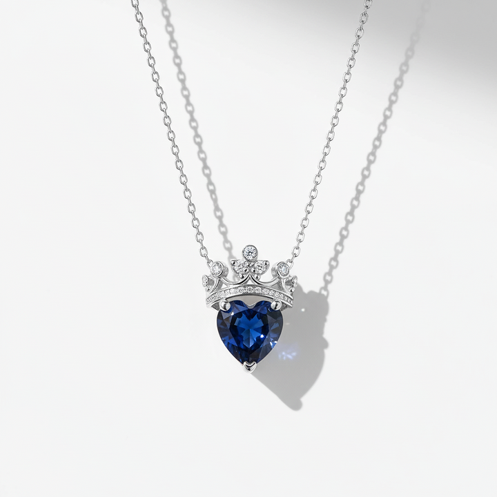 Heart-shaped blue gemstone necklace with a crown-like top on a white background
