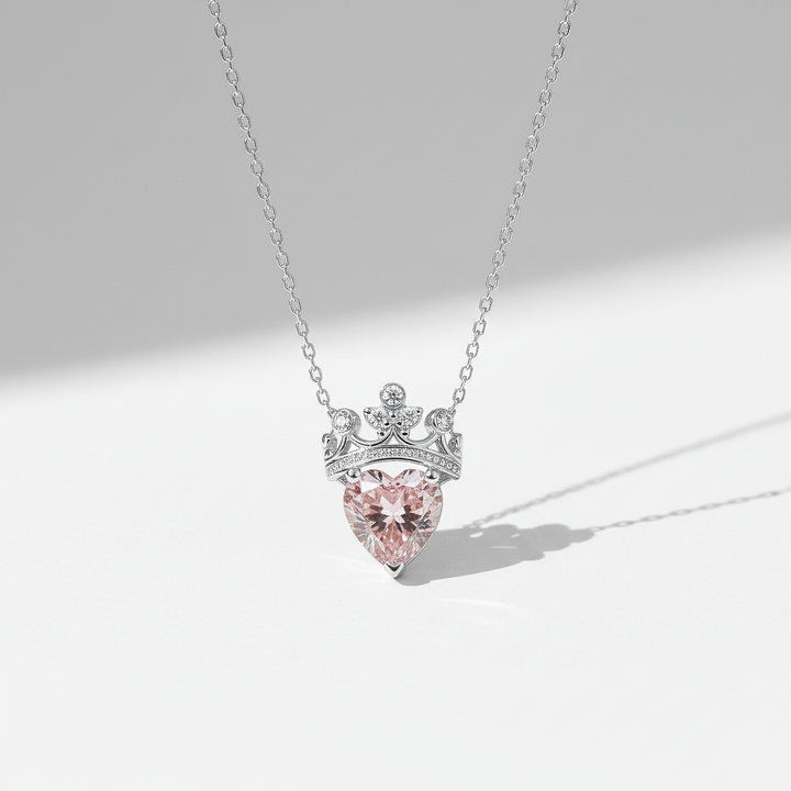 Necklace with a pink heart-shaped gem and silver crown-like top on a light gray background