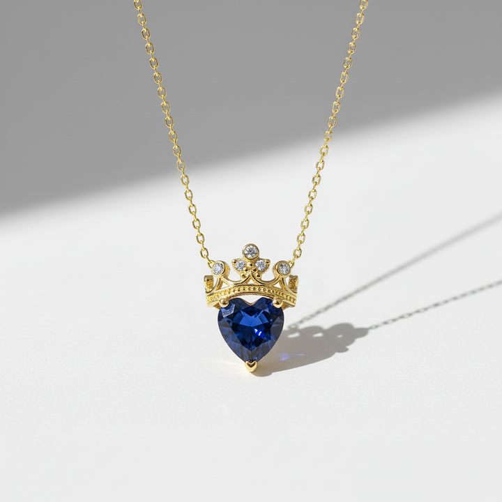 Gold necklace with a heart-shaped blue gemstone pendant on a light gray background