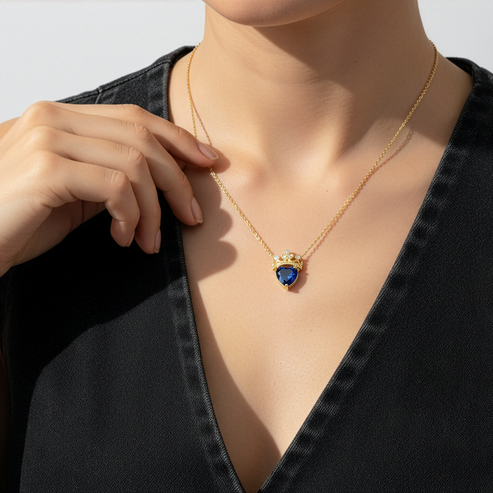Gold necklace with a blue heart-shaped pendant on a model wearing a black top.