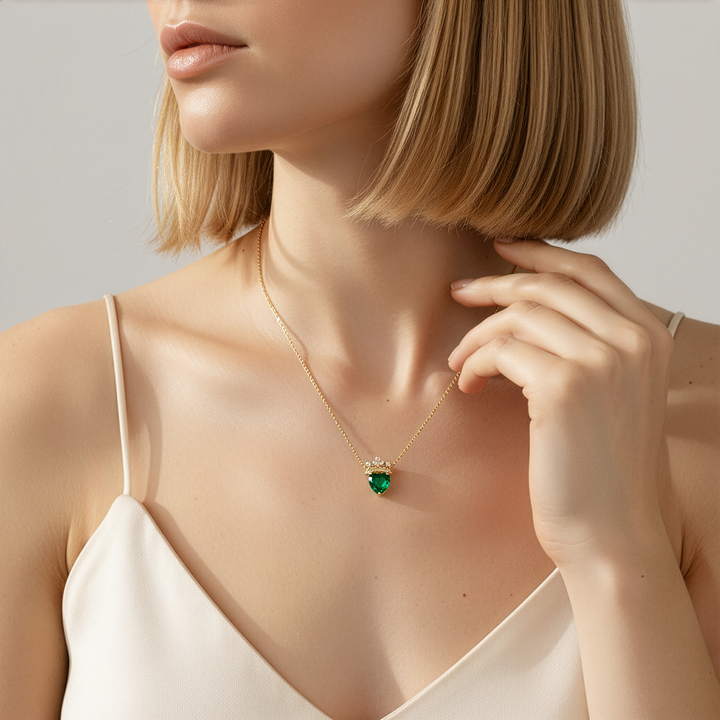 Woman wearing a gold necklace with a green heart pendant against a neutral background