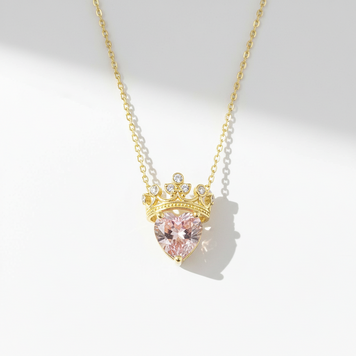 Necklace with a heart-shaped pink gemstone and gold crown pendant on a light gray background