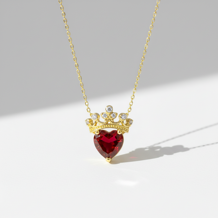 Necklace with a heart-shaped red gemstone and gold crown pendant on a light gray background