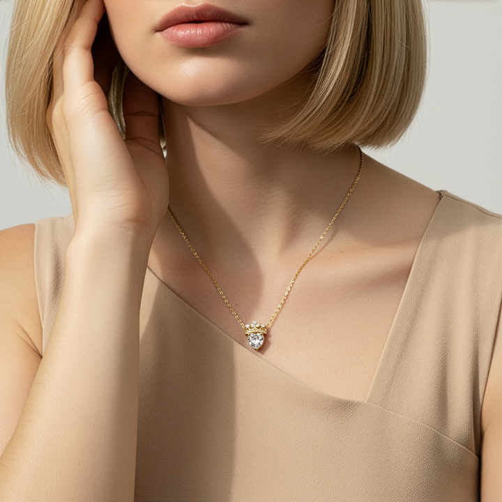 Woman wearing a gold necklace with a heart-shaped pendant against a neutral background
