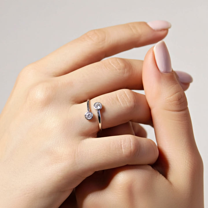Close-up of a hand wearing a silver ring with a small diamond on a neutral background