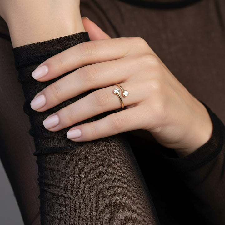 Hand wearing a gold ring with clear zirconia on a dark background