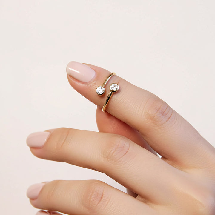 Gold ring with two diamonds on a finger against a light pink background