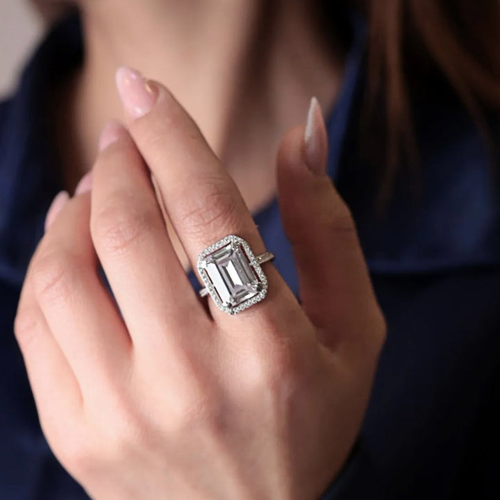 Close-up of a hand wearing an emerald-cut diamond ring with a dark background