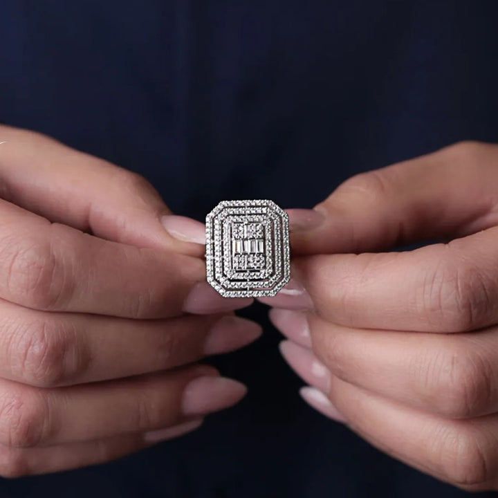 Silver ring with gemstones held between two hands against a dark background
