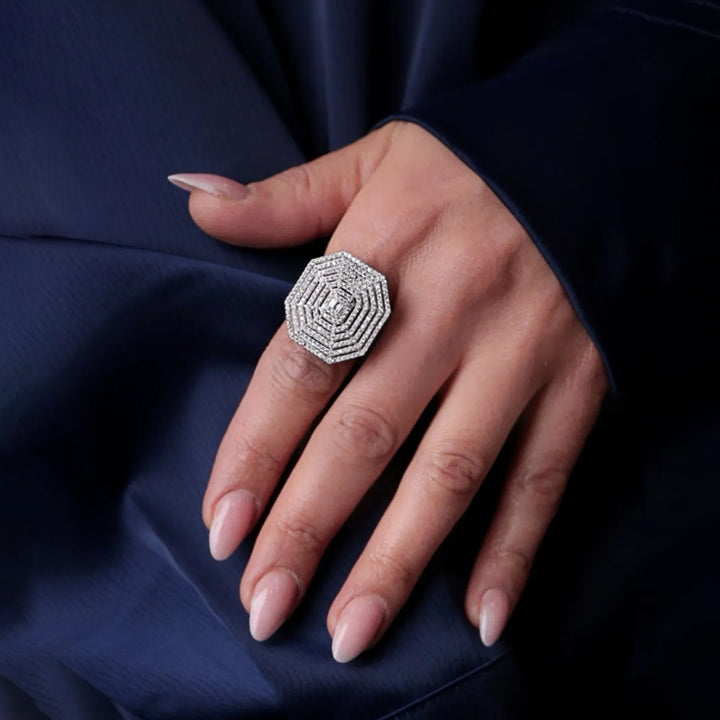 Hand wearing a silver ring with a diamond on a dark blue fabric background