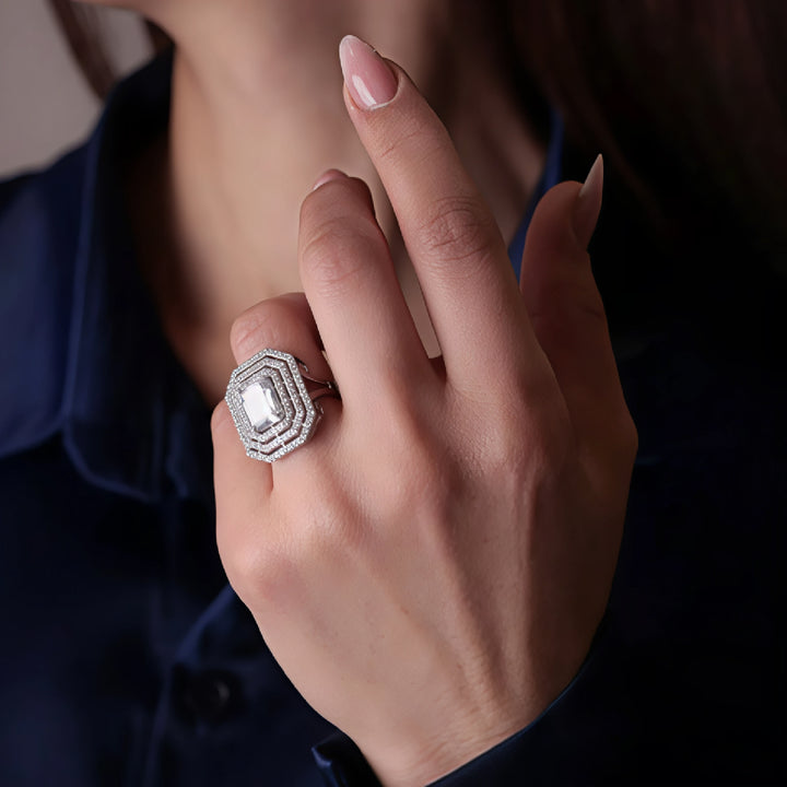 Hand wearing a decorative ring with a prominent gemstone against a dark background