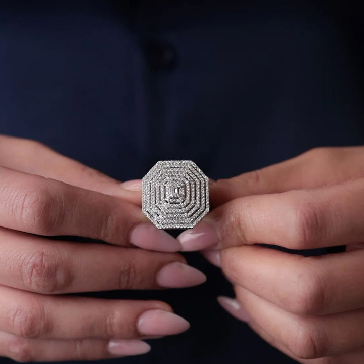 Close-up of hands holding a silver ring with intricate design against a dark background