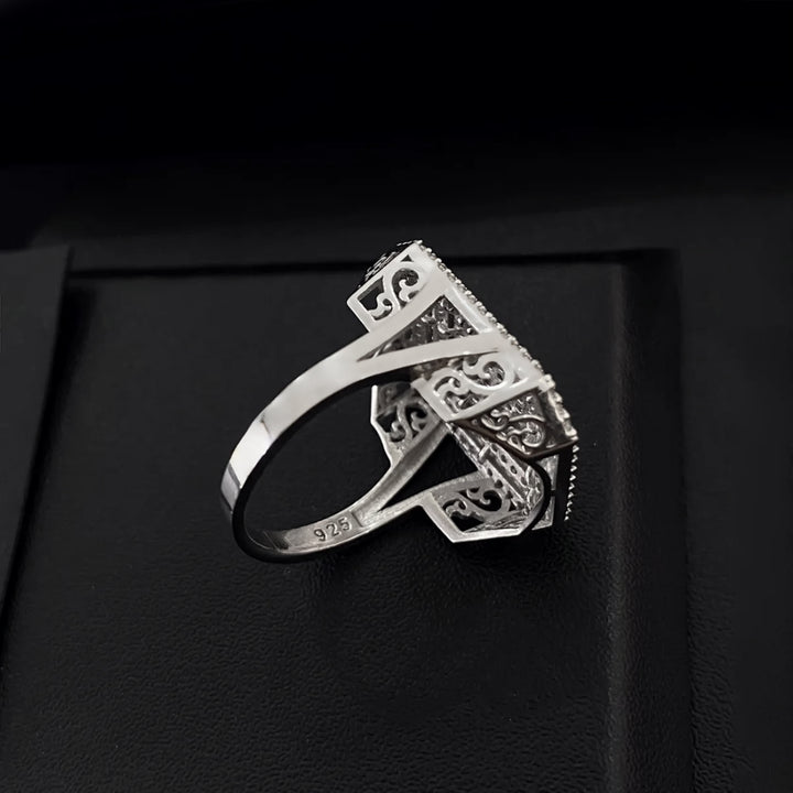 Silver ring with intricate design on a black background