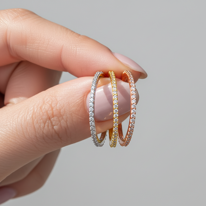 Three rings in silver, gold, and rose gold held between fingers against a neutral background