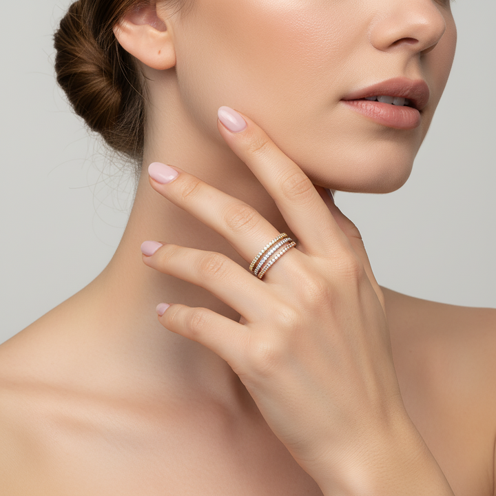 Close-up of a woman's hand with pink nail polish wearing multiple rings on a neutral background