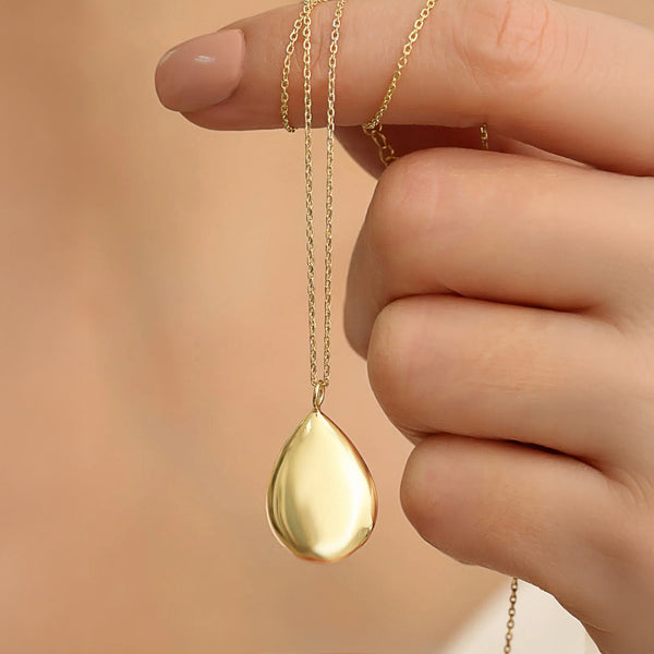 Gold teardrop pendant necklace held between fingers against a neutral background