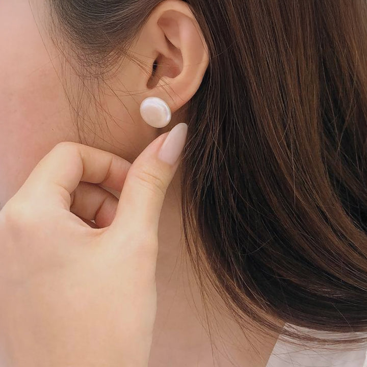 Close-up of a person wearing a pearl earring with a neutral background