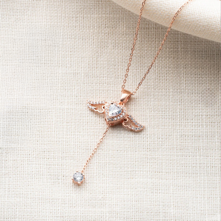 Rose gold necklace with heart-shaped pendant on a textured beige surface