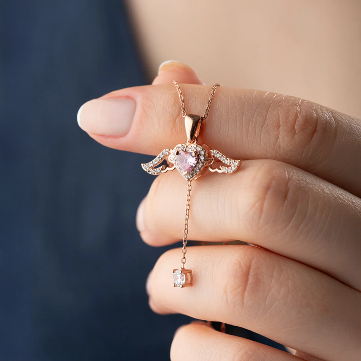 Rose gold necklace with heart-shaped pink gemstone pendant held by a hand against a blurred background
