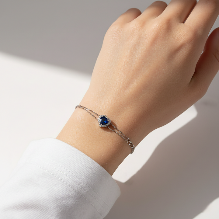Hand wearing a bracelet with a blue gemstone on a light background