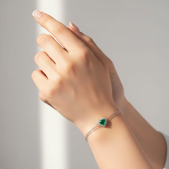 Hand wearing a bracelet with a green gemstone on a neutral background