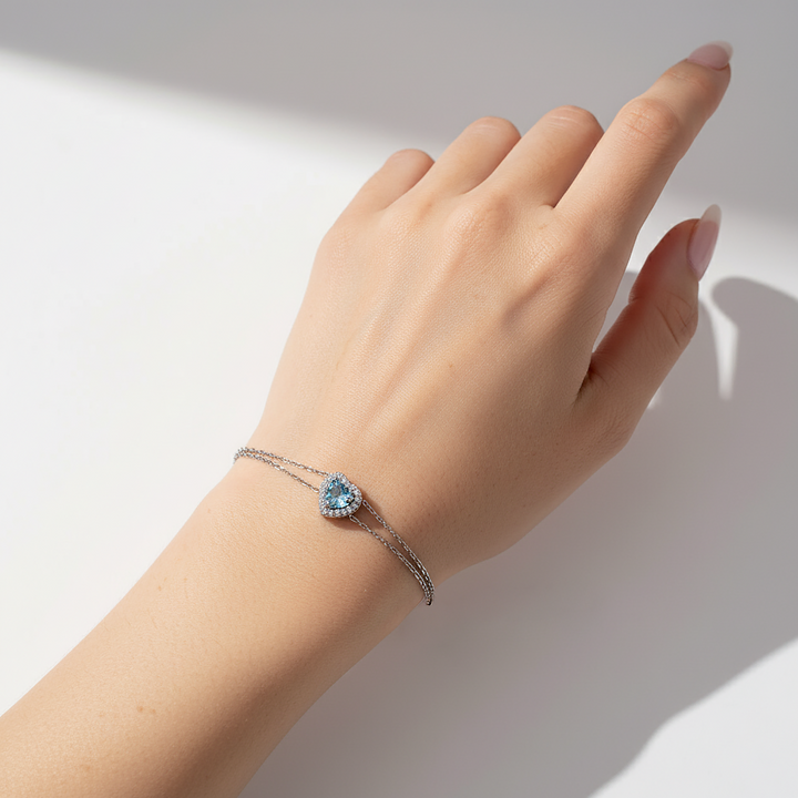 Hand wearing a bracelet with a blue gemstone on a neutral background