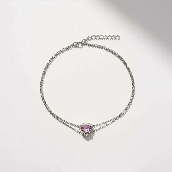 Silver bracelet with a pink heart-shaped charm on a light gray background