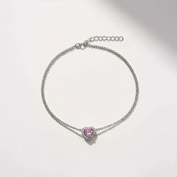 Silver bracelet with a pink heart-shaped charm on a light gray background