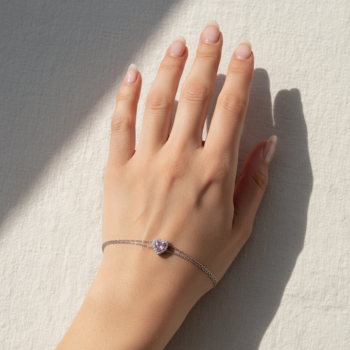 Hand wearing a bracelet with a pink gemstone on a light background