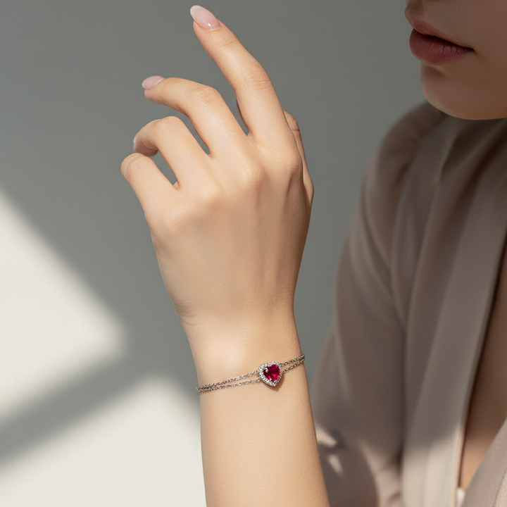 Hand wearing a bracelet with a red gemstone on a neutral background