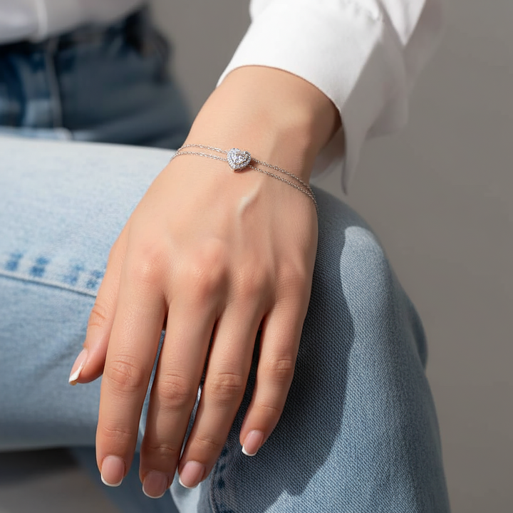 Hand wearing a silver bracelet with a clear stone, sitting on a gray surface.